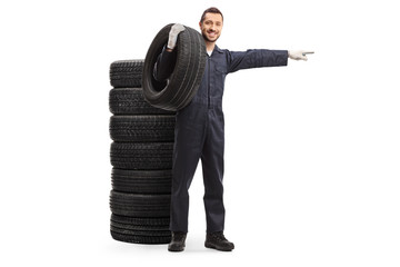 Poster - Auto mechanic standing next to a pile of tires, holding a tire and pointing