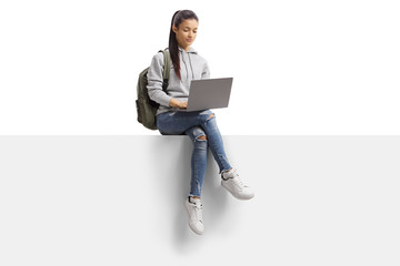 Wall Mural - Female student sitting on a blank board and using a laptop computer