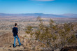 © The Wild in Focus - Hiker standing on cliff edge looking down at desert town and vast valley landscape