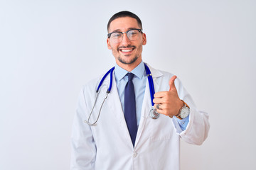 Wall Mural - Young doctor man wearing stethoscope over isolated background doing happy thumbs up gesture with hand. Approving expression looking at the camera showing success.