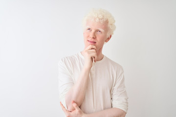 Wall Mural - Young albino blond man wearing casual t-shirt standing over isolated white background with hand on chin thinking about question, pensive expression. Smiling with thoughtful face. Doubt concept.