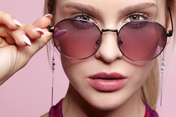 Close-up portrait of attractive young woman in tinted glasses on pink background