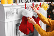 Woman Putting Gifts Into Christmas Socks Hanging On Fireplace At Home