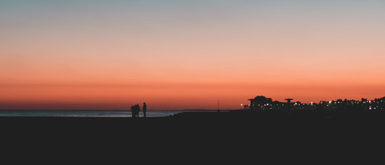 Atardecer soleado en la playa con silueta de personas y edificios