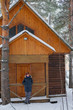 © evelinphoto - Snowboarding man sitting on snowy porch wooden rustic cottage in the winter woods.