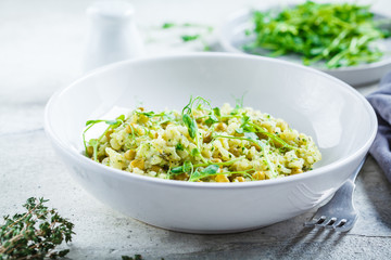 Green risotto with broccoli, green peas and sprouts in white plate. Healthy vegan food concept.