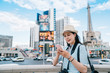 © PR Image Factory - Young female tourist using mobile phone on central square in front of famous tower in las vegas. girl backpacker holding cellphone chatting online with friends while travel in summer nevada usa.