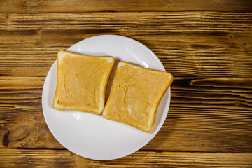 Two slices of bread with peanut butter on wooden table. Top view