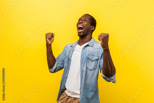 Cuadros en Lienzo Portrait of ecstatic overjoyed handsome man in denim casual shirt expressing winning gesture with raised fists and screaming, celebrating victory