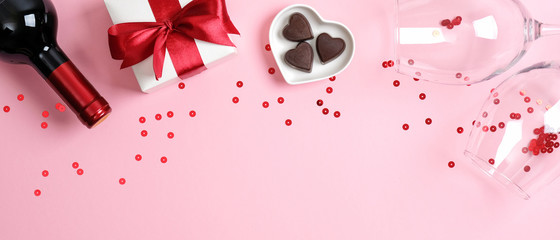 Valentine's day banner with bottle of wine champagne, gift box, two glasses and heart shaped candies on pink background with confetti. Romance, Love, Valentines day romantic dinner concept