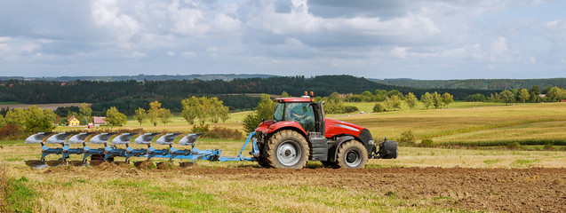 Farmer in red tractor preparing land with plow for sowing