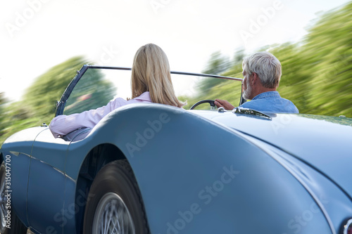 Rear View Of Mature Couple Enjoying Road Trip In Classic Open Top Sports Car Together