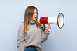 © luismolinero - Teenager girl with sweater over isolated blue background shouting through a megaphone