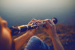 Close up of handsome caucasian bearded blond man sitting on cliff and playing clarinet.