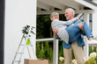 © LIGHTFIELD STUDIOS - mature man holding smiling woman in glasses near new house