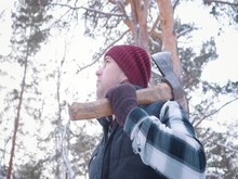 A Man Lumberjack Stands With An Ax On His Shoulder In A Snowy Forest. Close-up Bottom View Slow Motion