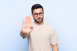 © luismolinero - Young handsome man with beard over isolated blue background making stop gesture with her hand