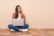 Teenager Student Girl Sitting On The Floor With A Laptop Looking Up While Smiling