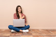 © luismolinero - Teenager student girl sitting on the floor with a laptop pointing to the side to present a product