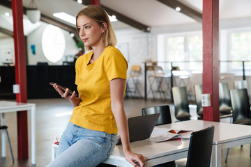 Canvas Print - Photo of focused blonde woman using cellphone while leaning on table