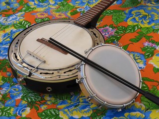 Two Brazilian musical instruments: samba banjo and tamborim with drumstick on a very colorful “chitao” fabric with large floral prints. They are widely used in samba and pagode ensembles.