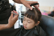 © thepoo - Little girl getting haircut by hairdresser at the barbershop.