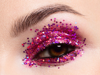 Close eye with colorful eyeshadow. Macro shot of opened human female eye. Woman with evening beauty makeup. Girl with perfect skin and eyebrow. Women cosmetics, extremely long eyelash and red glitter