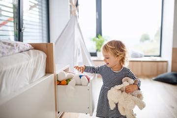 Cute small toddler girl indoors in bedroom playing.