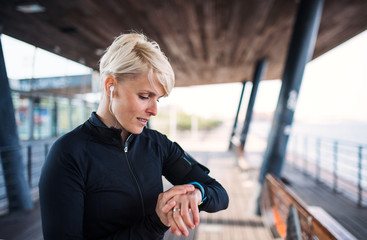 A portrait of young sportswoman with smartwatch outdoors, self-tracking.