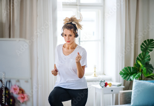 Fotomural Young woman with headphones doing exercise in bedroom indoors at home