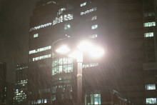 Rain Falling Around Streetlamp Below Urban Highrise Buildings At Night