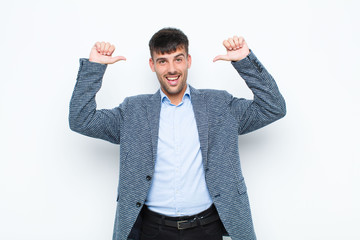 young handsome man feeling proud, arrogant and confident, looking satisfied and successful, pointing to self against white wall