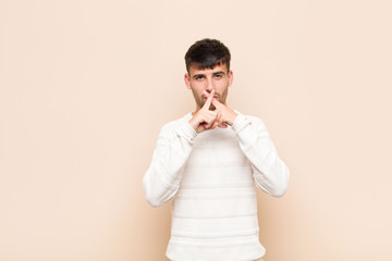 young handsome man looking serious and displeased with both fingers crossed up front in rejection, asking for silence against warm wall