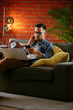 © JustLife - Young man working from home. Businessman at home on sofa with laptop and phone.