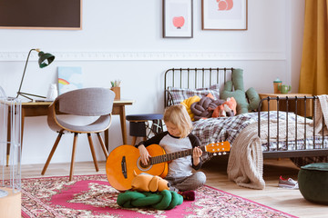 Cute blond girl sitting on the floor of her trendy bedroom,learning how to play a guitar