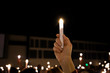 One single hand arm holding up a LED candle amongst a crowd of lights at a candlight service vigil