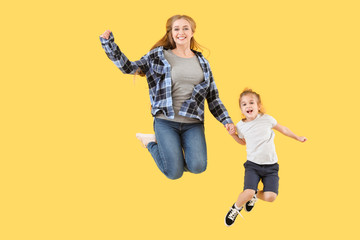 Wall Mural - Jumping young woman and her little daughter on color background