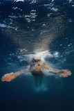 Fototapeta Łazienka - Professional swimmer moving fast in ocean water deep blue color on background, underwater shot