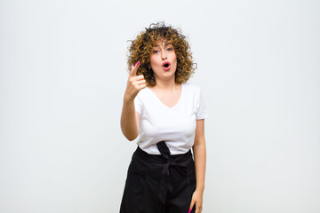 young pretty woman pointing at camera with an angry aggressive expression looking like a furious, crazy boss against white wall