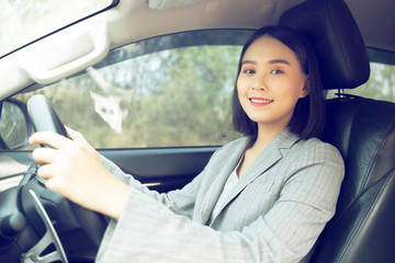 Safety driving concept, Smiling happy young  Chinese Thai Asian businesswoman driving a car in town, Confident and beautiful girl. Rear view  woman in business suit wear looking over her shoulder