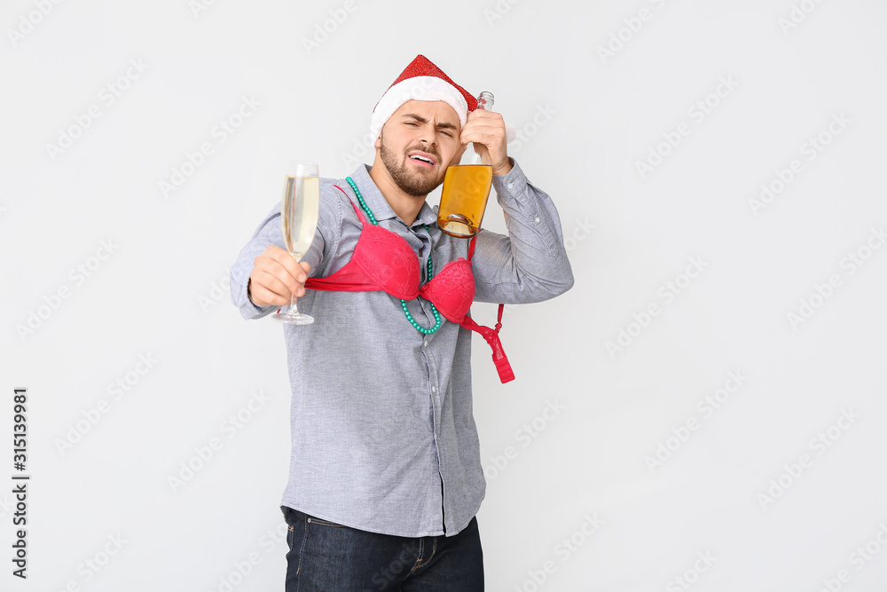 Drunk man with Santa Claus hat and champagne on light background