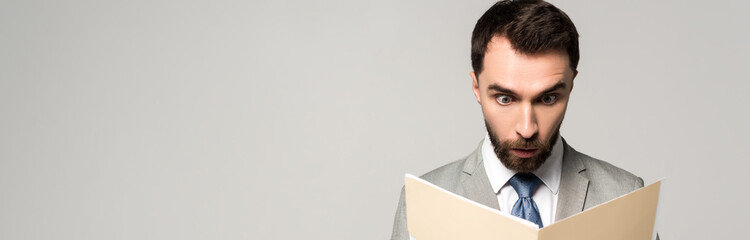 panoramic shot of shocked businessman looking at documents in paper folder isolated on grey