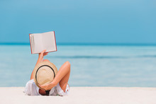Portrait Of A Young Woman Relaxing On The Beach, Reading A Book