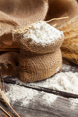 Flour in burlap bag with wheat ears on wooden background. Food background 