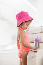 Toddler Girl In Bathing Suit Using Digital Tablet At Sofa