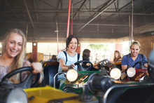 Enthusiastic Friends Riding Bumper Cars At Amusement Park