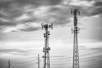 A black and white moody atmospheric shot of two cellular network towers and overhead power cables. Urban street furniture with copy space to left.