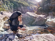 © Trevor Adeline/Caia Image - Young woman with backpack hiking, washing hands at sunny stream