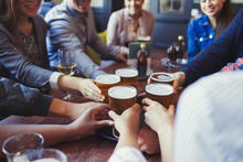 Friends Reaching For Beer Glasses On Bar Table