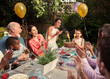 © Robert Daly/Caia Image - Multi-ethnic multi-generation family clapping celebrating birthday fireworks cake at patio table